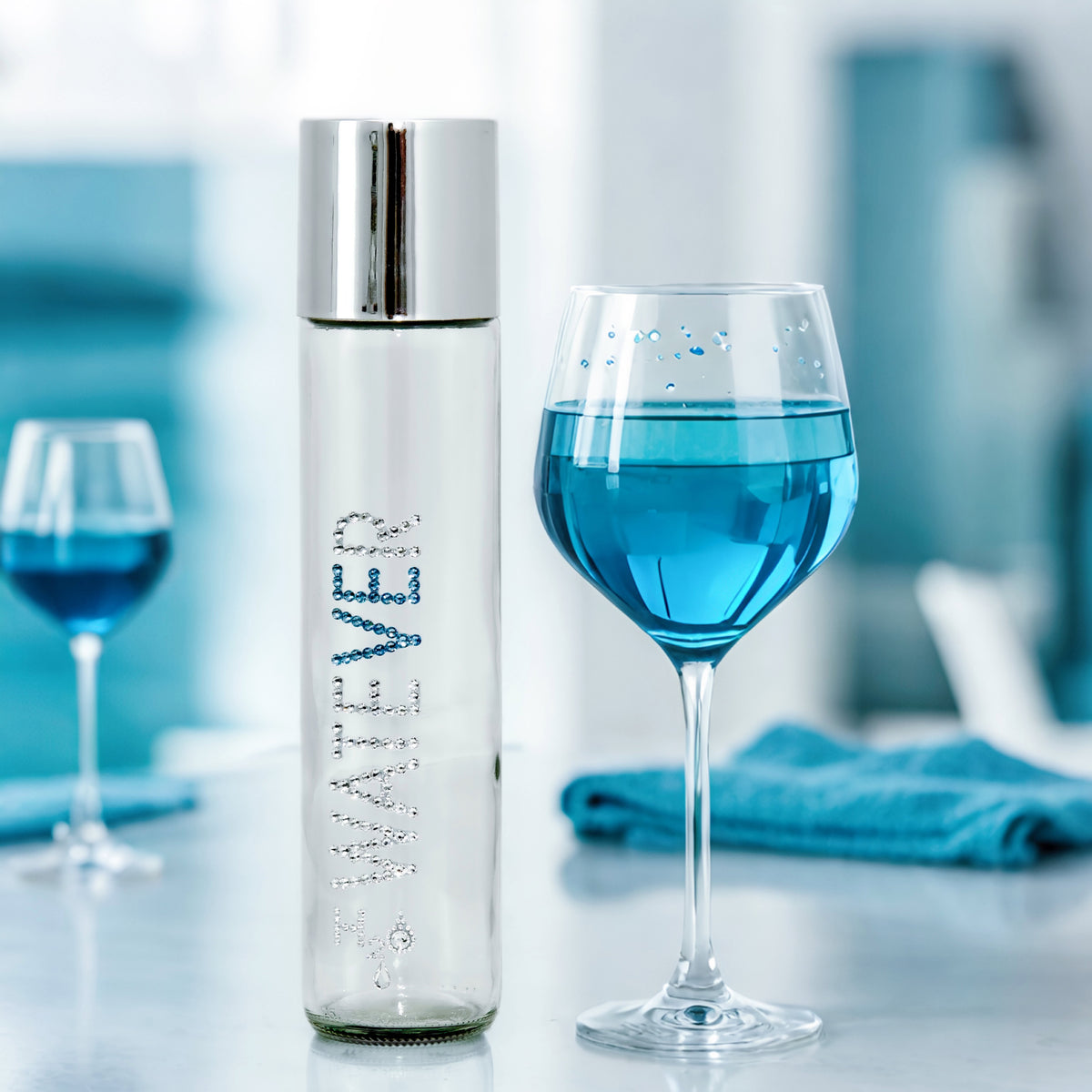 Watever glass water bottle with clear and blue crystals lettering and silver cap in blue table setting